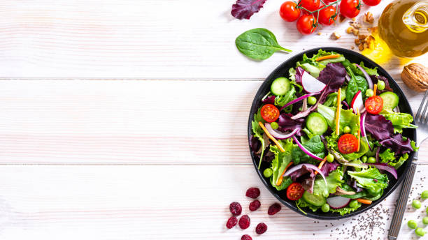 Fresh vegetables salad plate on white table. Copy space Vegan food: overhead view of a healthy fresh vegetables salad plate shot on white table. An olive oil bottle, chia seeds, walnut, cherry tomatoes, spinach leaves and green peas are around the salad plate. The composition is at the right of an horizontal frame leaving useful copy space for text and/or logo at the left. High resolution 42Mp studio digital capture taken with Sony A7rII and Sony FE 90mm f2.8 macro G OSS lens olive oil photos stock pictures, royalty-free photos & images