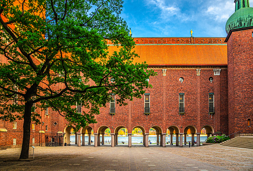 Courtyard in Stockholm City Hall building Stadshuset of Municipal Council and Nobel Prize with view of Lake Malaren through arches, brick walls, tiled roof and green tree, Sweden