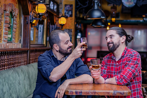 Two male friends toasting and drinking whiskey together at the pub. Cheers.