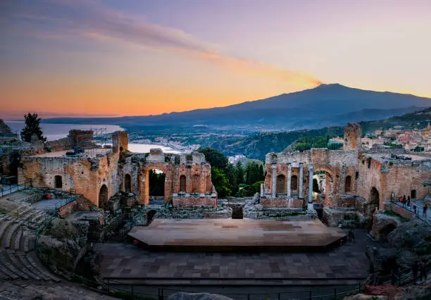 Photo of Ruins of Ancient Greek theatre in Taormina on background of Etna Volcano, Italy. Taormina located in Metropolitan City of Messina, on east coast of island of Sicily