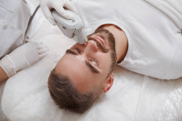 Handsome man getting facial skincare treatment at salon Close up of a bearded man enjoying getting laser facial treatment by professional cosmetologist Removal and Skincare stock pictures, royalty-free photos & images