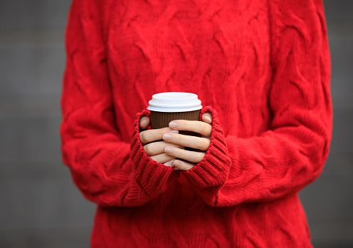 Unrecognizable person in a red pullover holds a brown cup of hot drink