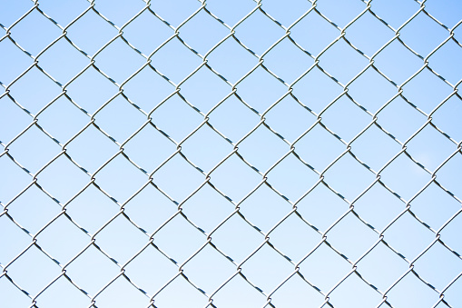 Closeup chain link fence, light blue abstract background with copy space, horizontal composition