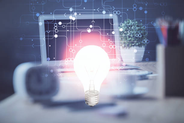 istock Computer on desktop in office with bulb icon hologram. Double exposure. Concept of idea. 1289089026