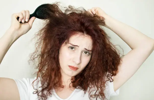 Young woman trying to comb her curly hair