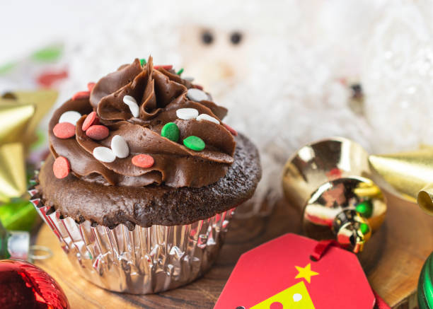 istock A Chocolate Christmas cupcake sits on a board surrounded by gift tag, bows, ornaments, and a Santa. 1289097867