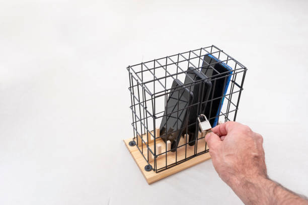 hand opening or closing the lock on a cage with three mobile phones locked in a cage with a padlock, concept of social isolation or phone abuse and social networking, white background, horizontal - prison cell imagens e fotografias de stock