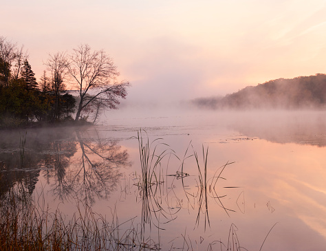 Mist comes off a pond on a golf course during a fiery sunrise
