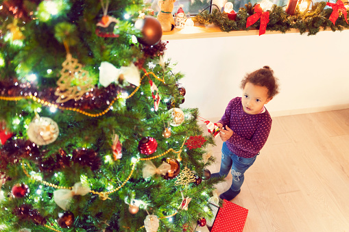 An African-American ethnicity, cute girl decorating Christmas tree.