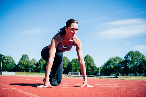Surface level front view of mid adult Caucasian female athlete in crouch position with hands on starting line and looking straight ahead.