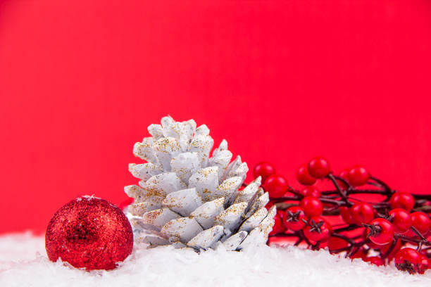 Red kokina flower, white pine cone and bright red new year ornament on red background and snowy backdrop for Christmas stock photo