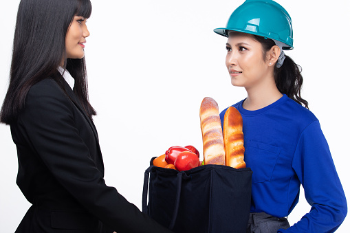 Asian Woman is Food Delivery service, Female send bread and fruit in fabric bag and smile to office business woman, white background isolated copy space