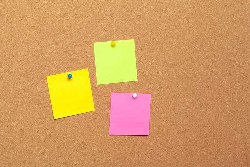 colorful sticky notes with pushpins and blank space, on cork background. creative photo.