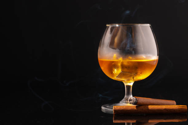 istock Glass of whisky and lighted cigar on black background 1289129764