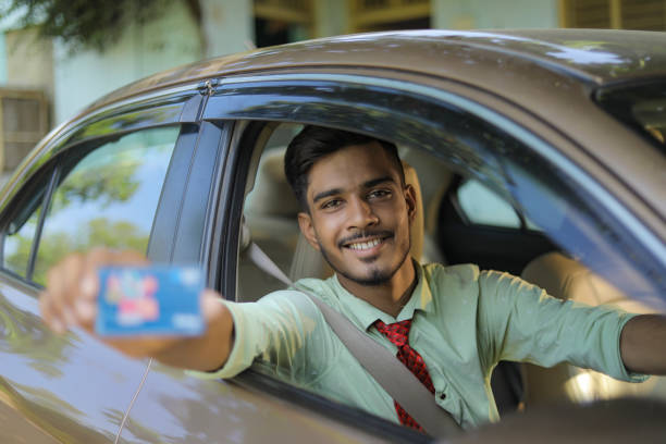 istock Young Indian man sitting inside his new car showing card 1289129854