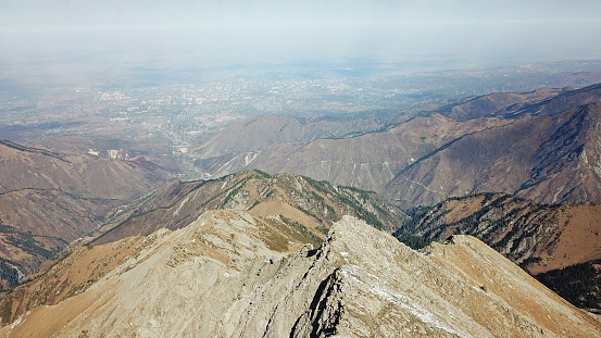 Mountain tops covered with snow. View from a drone. Huge rocks lie on the steep slopes of the mountains. Snow-capped peaks can be seen in the distance, sometimes flashing the city in the smog.