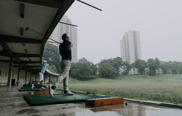 asiatische chinesische reife mann schwingt seinen golfschläger auf driving range - golf power golf course challenge stock-fotos und bilder