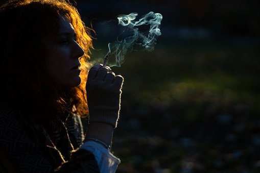 Young woman smoking a cigarette in the dark. Copy space.