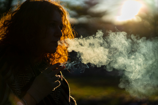 Young woman smoking a cigarette outside. Copy space.