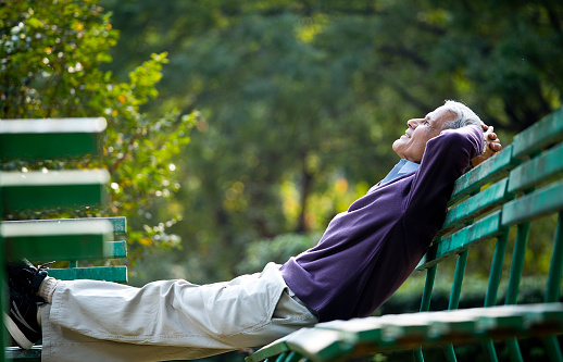 Thoughtful senior man relaxing with hands behind head at park bench