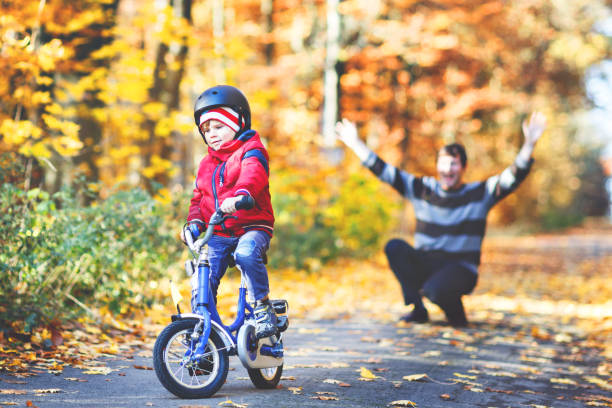 自転車で移動を学ぶ小さな子供の男の子。彼の父親は息子に自転車を教えています。幸せな男と子供。アクティブな家族のレジャー。自転車にヘルメットをかぶった子供。子供のコンセプト� - park and ride ストックフォトと画像