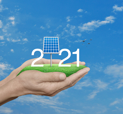 2021 white text with solar cell on green grass field in man hands over blue sky, white clouds and birds, Happy new year 2021 ecological cover concept