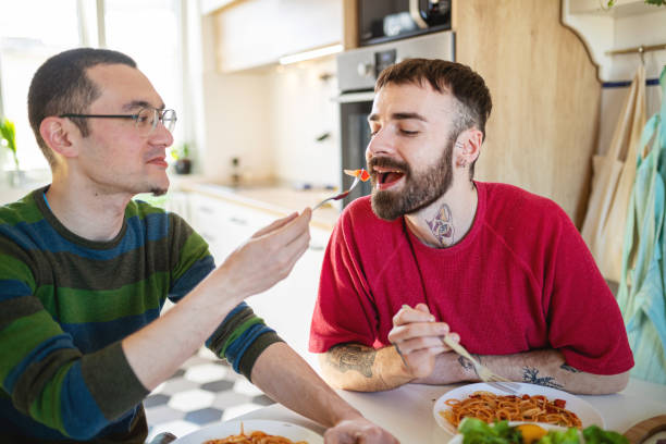 istock Young man taking a bite from his boyfriend's fork at the dining table 1289139927