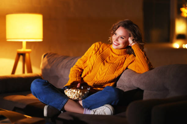 istock Positive woman with popcorn resting on sofa and watching TV 1289140768