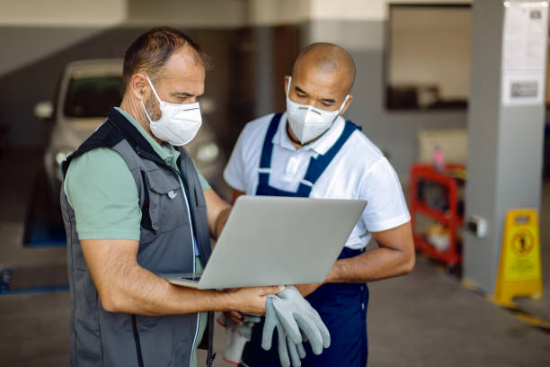 istock Two auto mechanics wearing face masks while working on laptop in a workshop. 1289140832