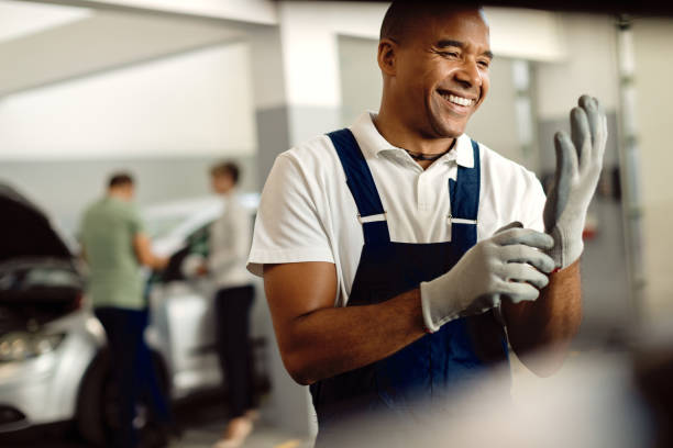 istock Happy black auto mechanic using gloves while working at repair shop. 1289140868