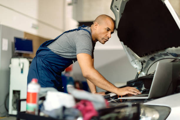 istock Black mechanic using laptop while running car diagnostic in a repair shop. 1289143786