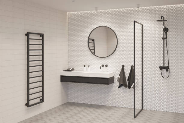une salle de bains lumineuse avec un miroir rond au-dessus d’un lavabo noir et blanc, avec deux serviettes terry, une cloison en verre, une douche, un rail de serviette chauffé noir. - installation domestique photos et images de collection