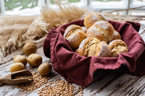 Breakfast rolls with grains and potatoes in a bowl on a wooden table. Part of a seriesBreakfast rolls on a wooden table made of flour and potatoes. Pampas grass in the background. Part of a series.