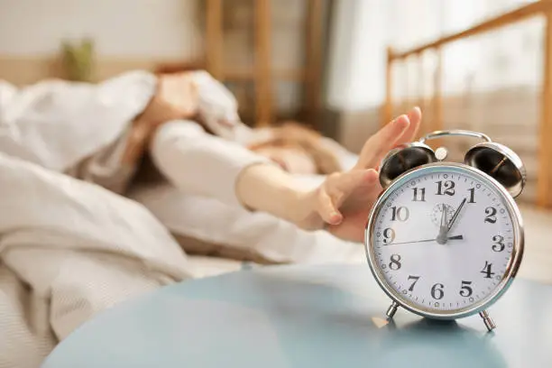 Close-up of alarm clock ringing on the table with woman sleeping in bed in the background