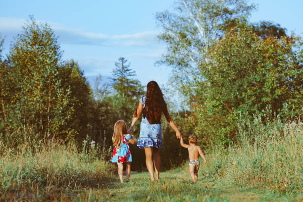 Mother walking with her children along a path, holding hands. Mom is with an 8 year old girl and 16 month old baby, with brown colors in their clothes. An autumn picture
