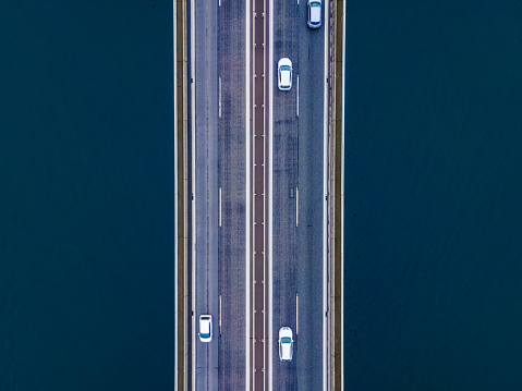 Top down aerial view of a highway on a bridge over the sea, cars driving on the road.