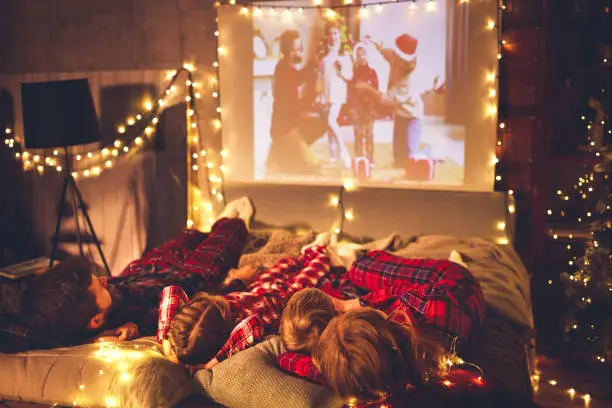 happy family in checkered pajamas: mother father and children watching projector, TV, movies with popcorn in christmas holiday evening   at home