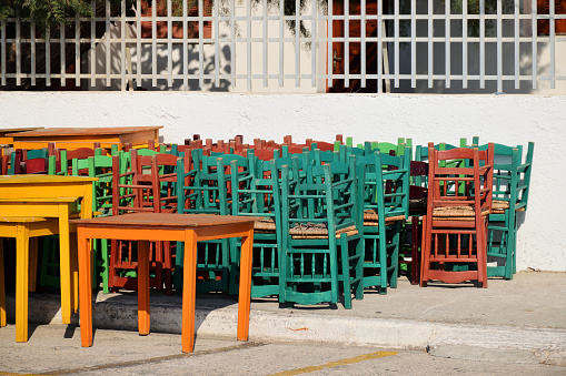 Chairs stack, closed restaurant Covid-19 Pandemic lockdown. Wooden tavern seats stacked outdoor. Crete Island, Greece