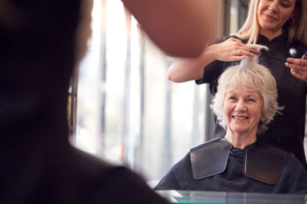 donna anziana con i capelli tagliati da stilista femminile nel parrucchiere - tagliare i capelli foto e immagini stock