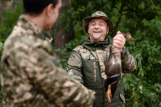 szczęśliwy myśliwy człowiek pokazuje pobrane wild duck do syna. - hunting two people camouflage rifle zdjęcia i obrazy z banku zdjęć