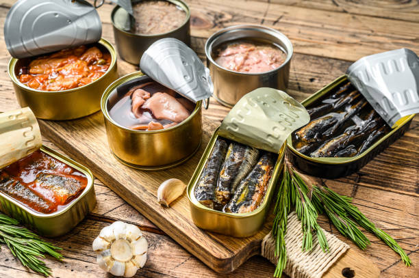 金属缶に入った様々な缶詰の魚介類。木製の背景。トップビュー - can ストックフォトと画像