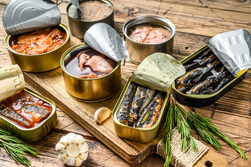 Various canned  fish and seafood in a metal cans. Wooden background. Top view.