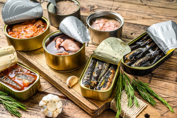 различные рыбные консервы и морепродукты в металлических консервах. деревянный фон. вид сверху - canned food стоковые фото и изображения