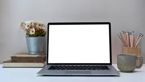 istock Front view of simple workspace with white blank screen monitor computer laptop and equipment on white desk. 1289157724