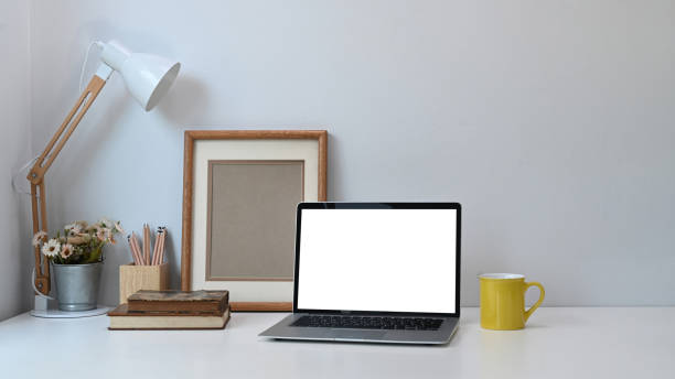 istock Comfortable working place with blank screen laptop, notebooks, coffee cup and tree pot on white table. 1289157804