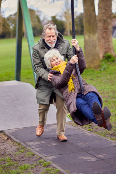 公園の遊び場でスイングで遊んで楽しんでいるシニアカップル - senior adult fun autumn senior couple ストックフォトと画像