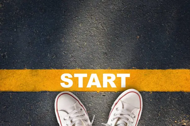 Photo of Start written on yellow line on asphalt road with sport shoe