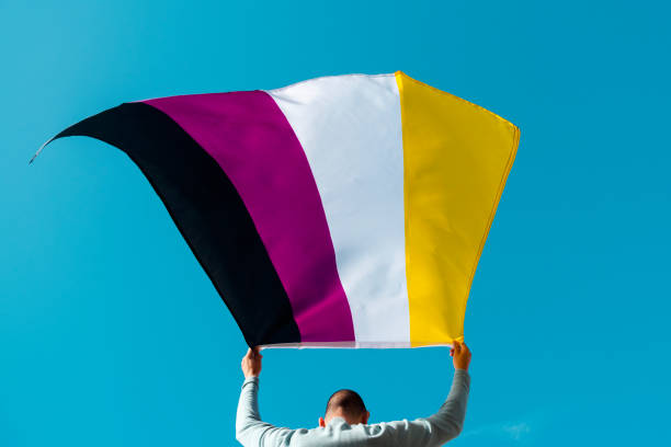 person waving a non-binary pride flag closeup of a young caucasian person, seen from behind, waving a non-binary pride flag on the air non binary gender photos stock pictures, royalty-free photos & images