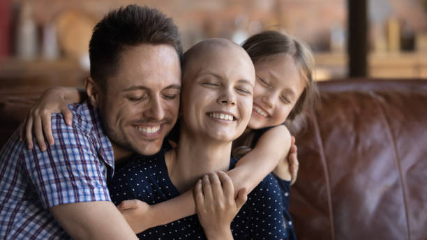 Husband dad and daughter cuddling wife mom fighting against cancer Loving and caring. Affectionate happy young husband dad and school age daughter kid sitting on couch supporting cuddling warm tight beloved smiling millennial wife mom fighting against cancer disease cancer illness stock pictures, royalty-free photos & images