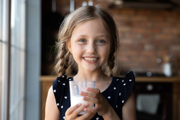 cheerful little girl with milk mustache holding glass of yoghurt - milk mustache imagens e fotografias de stock